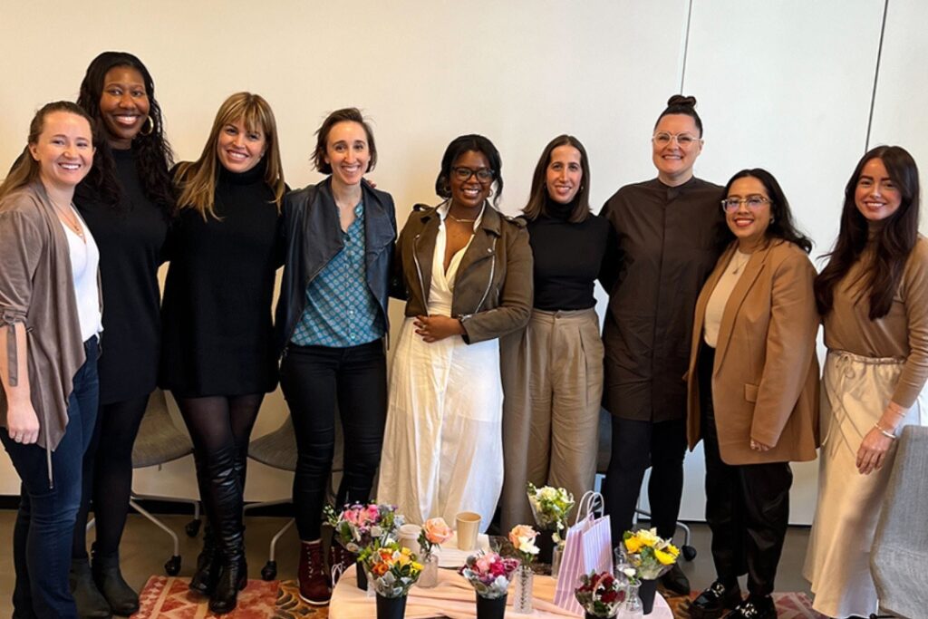 Several members of the Women@Industrious employee resource group are gathered for an event, huddled together and smiling for a photo.